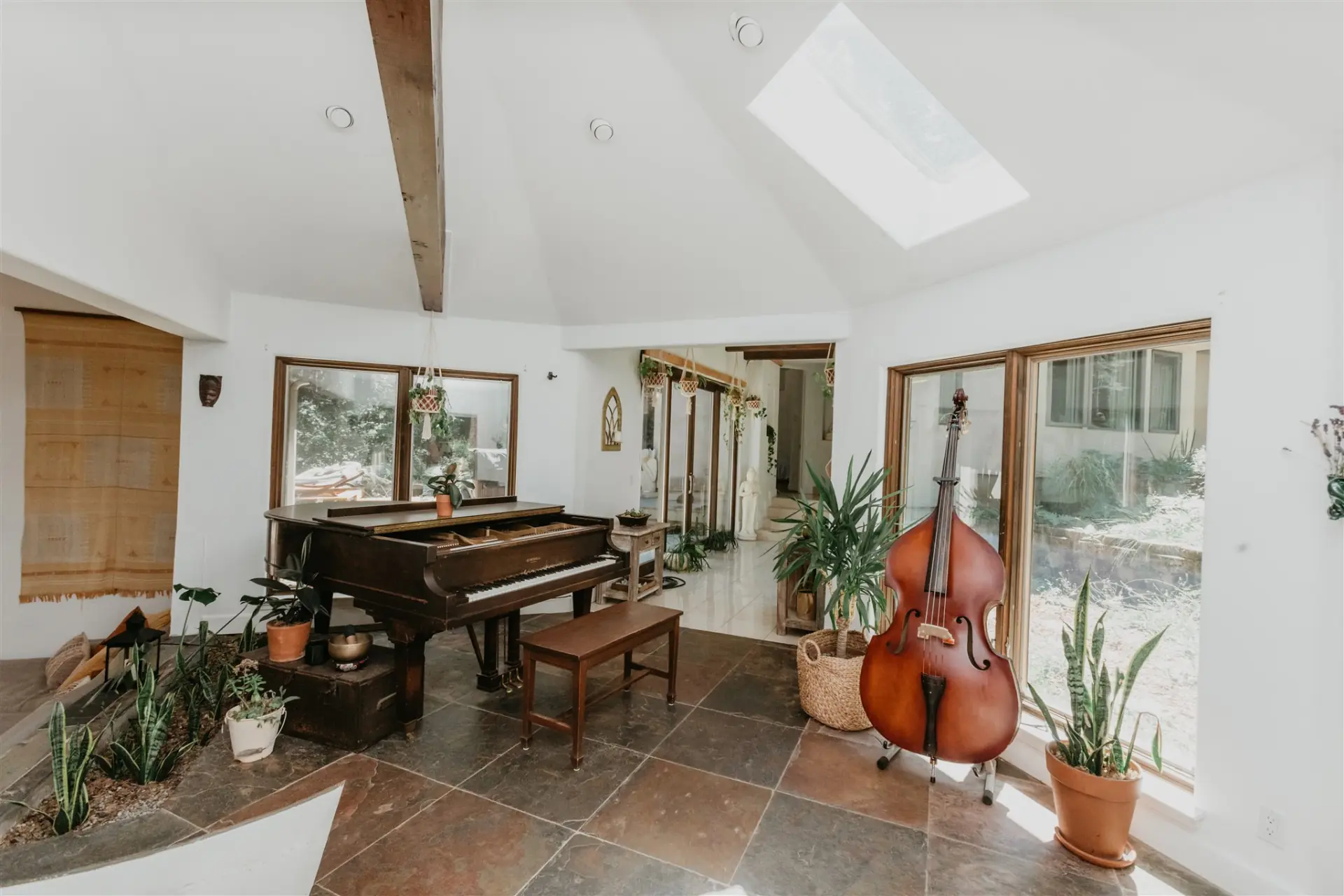 A light-filled room with a grand piano and upright bass, opening onto the trees