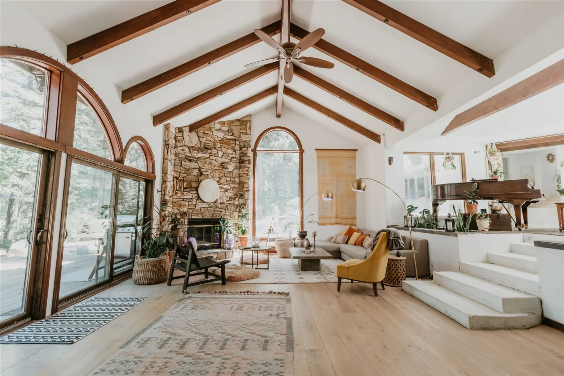 The great room from the entry, sunlight across the rug and the stone fireplace beyond