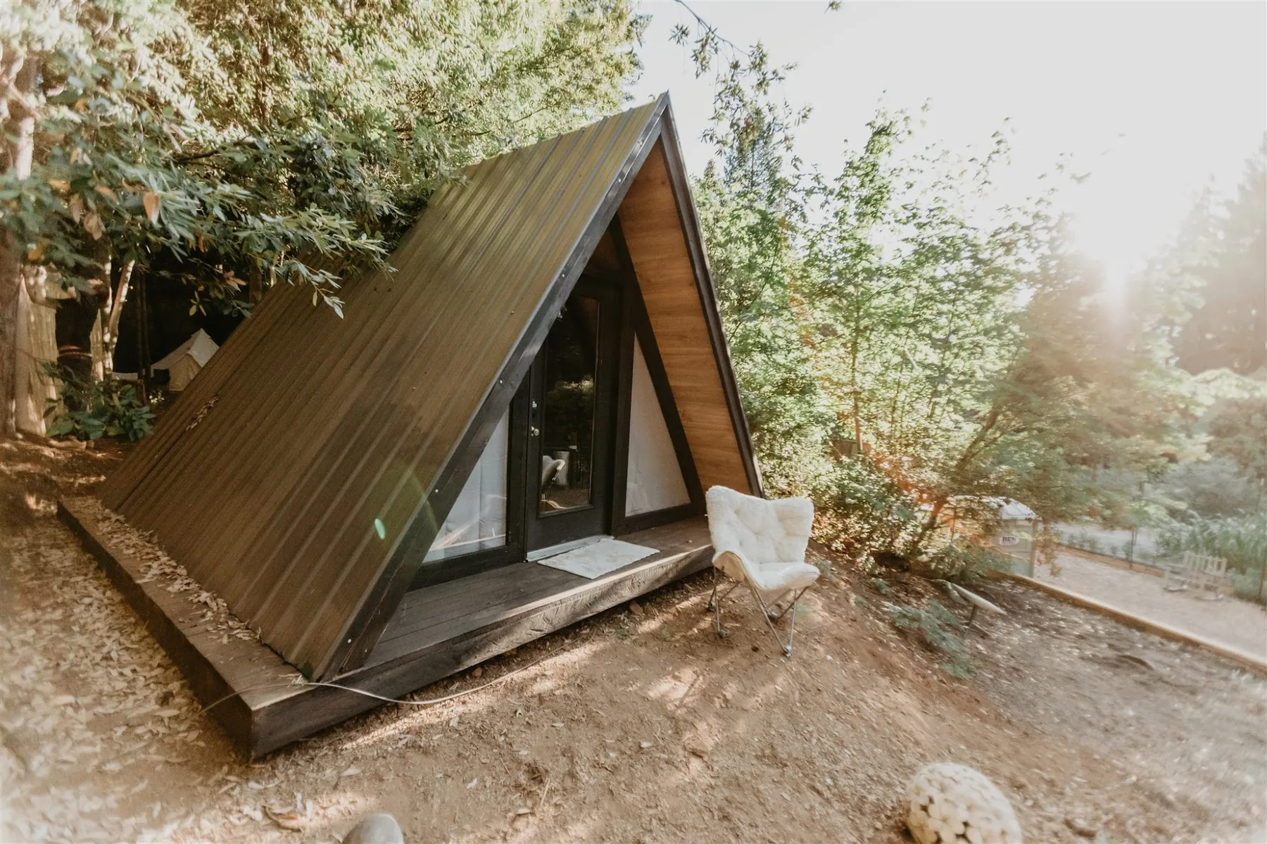 The dark timber A-frame cabin set into the slope among young trees