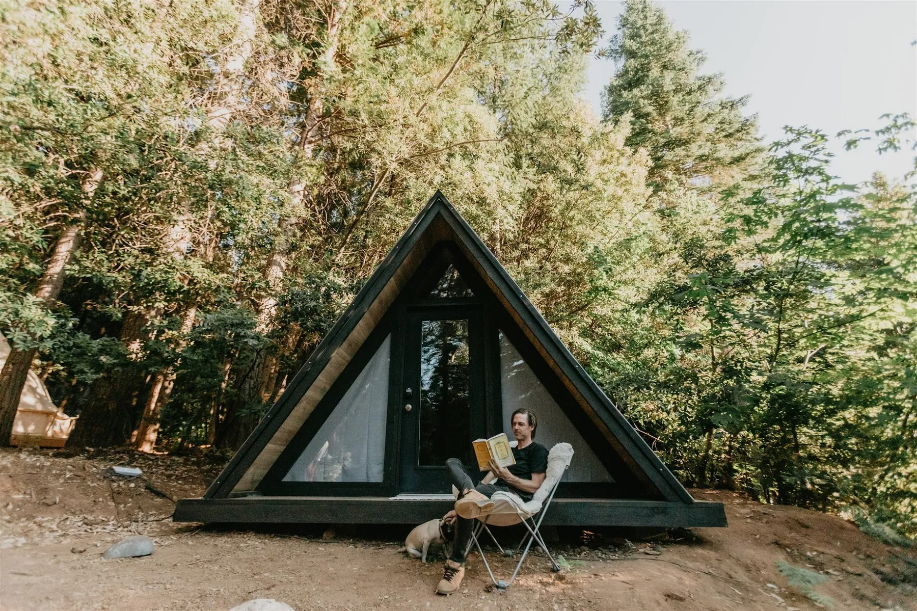 The A-frame cabin in the trees, a guest reading in a chair outside the door