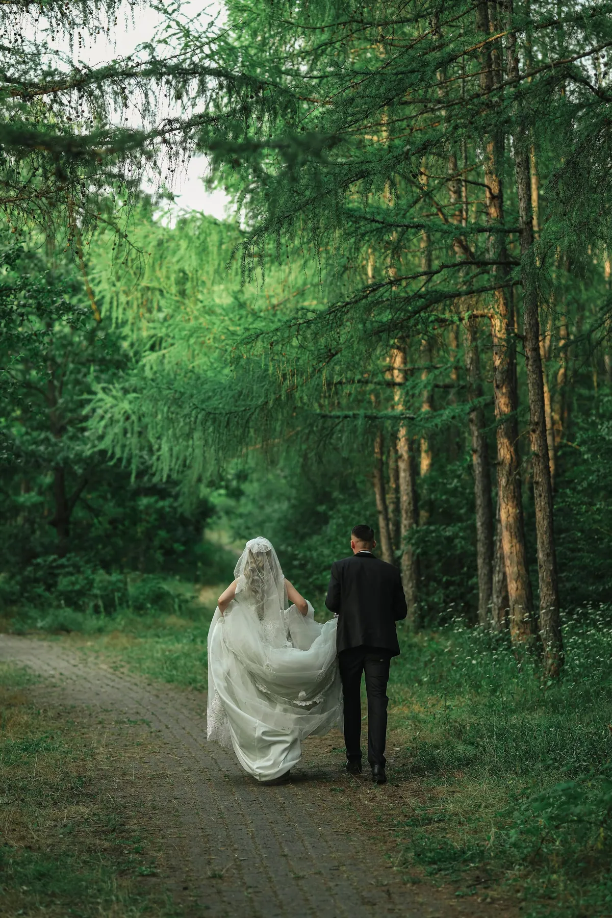 A bride and groom walking away down a path into the forest