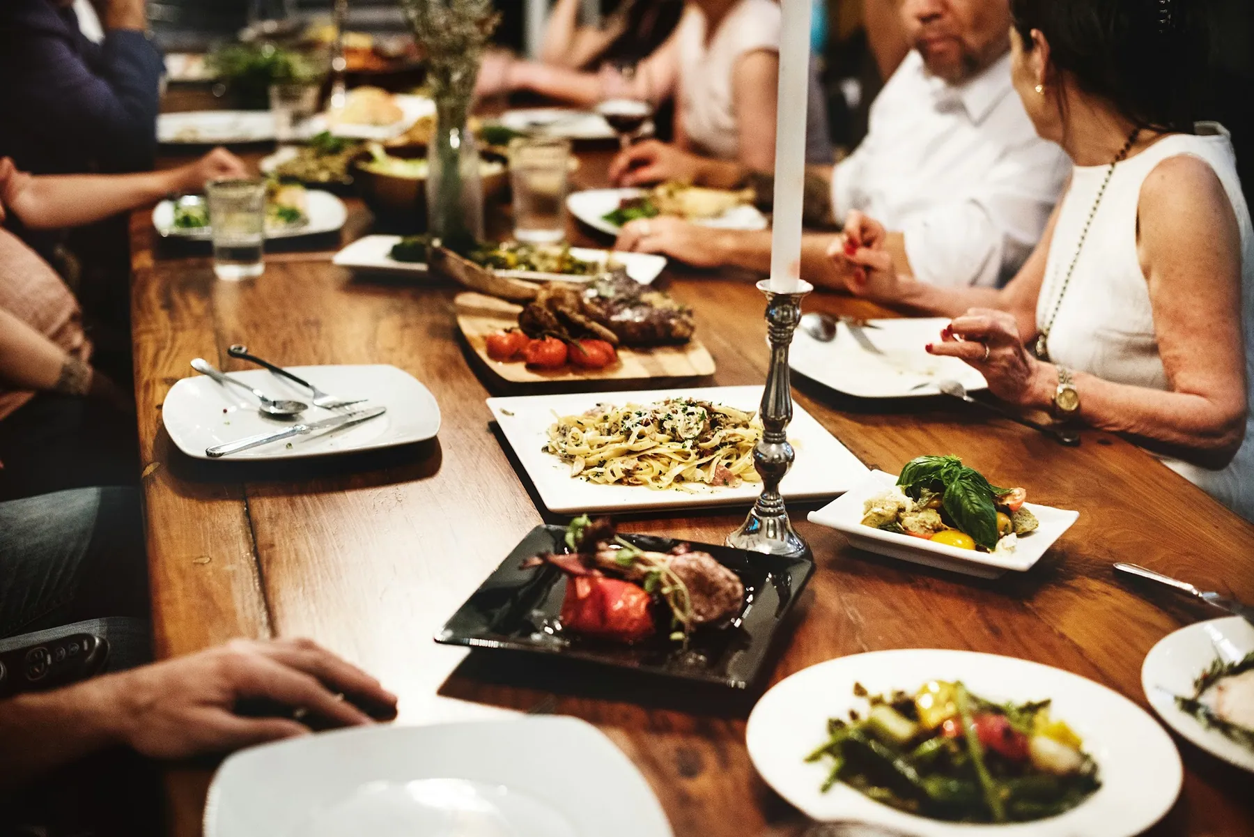 Guests sharing a long family-style dinner at a candlelit wooden table