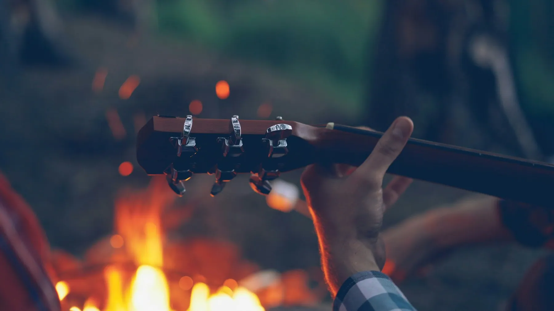 The headstock of an acoustic guitar held beside a campfire at night