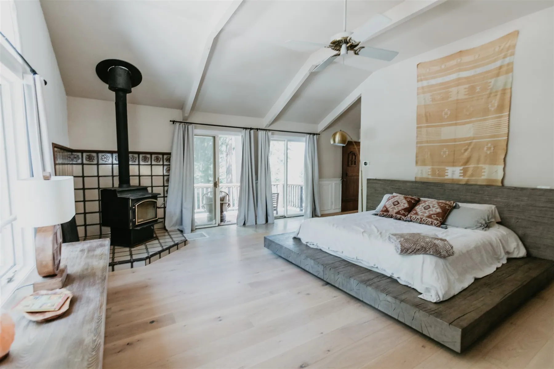 A bedroom with a wood-burning stove, platform bed and doors onto the balcony