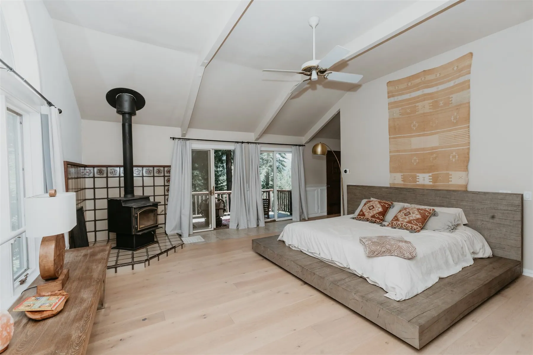 A lodge bedroom with a wood-burning stove, platform bed and doors onto the trees