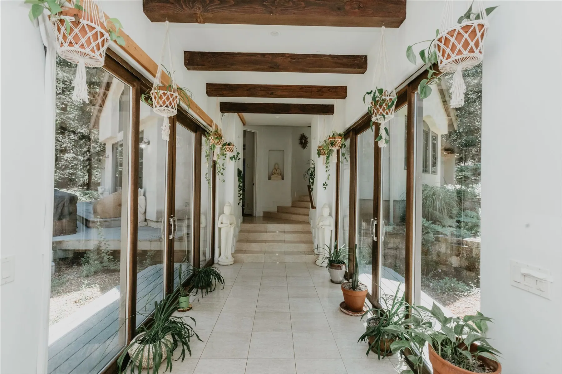 A glass-walled breezeway lined with hanging plants connecting the wings of the lodge