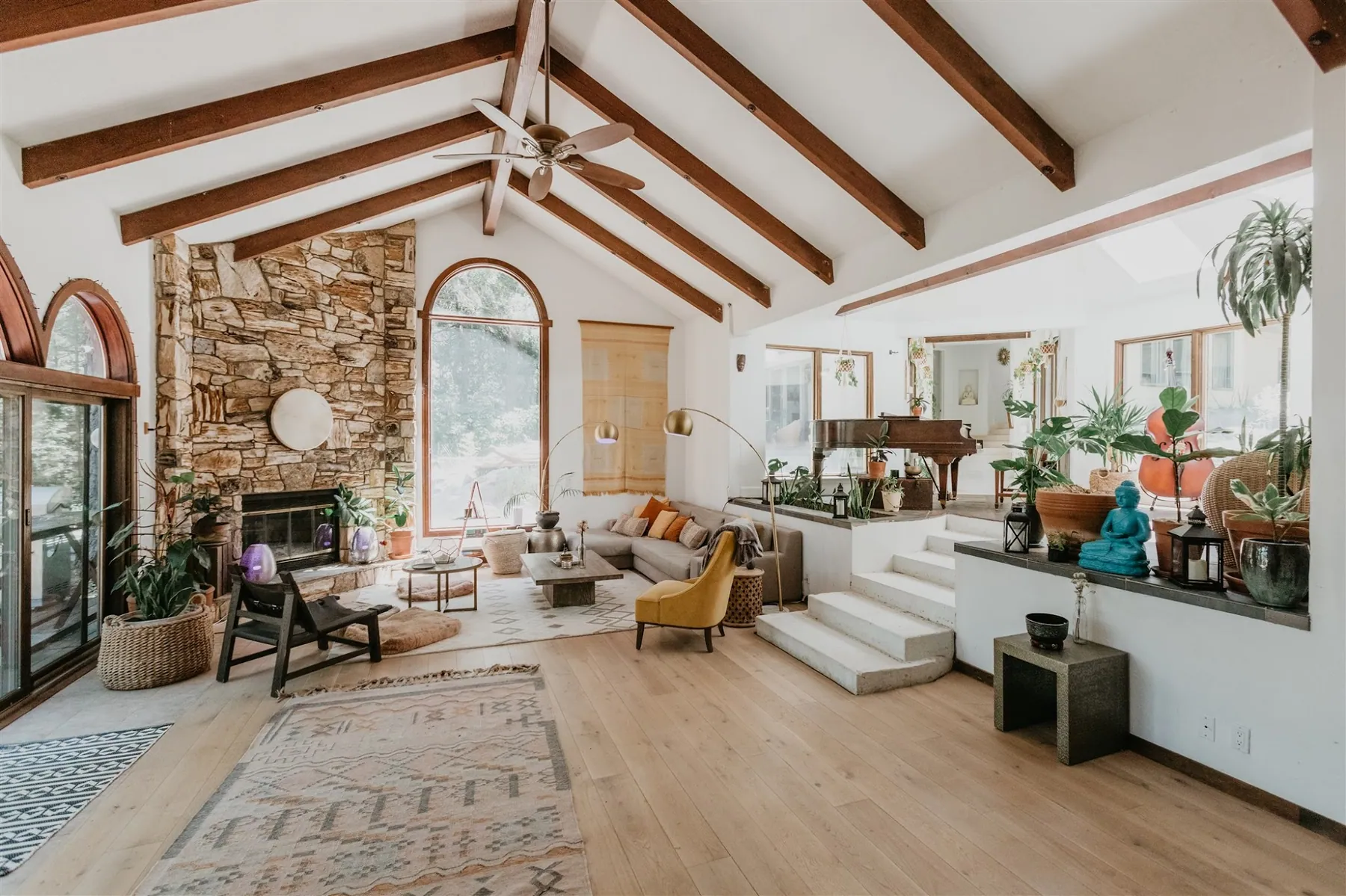 The great room with a stone fireplace, arched windows and vaulted wood beams