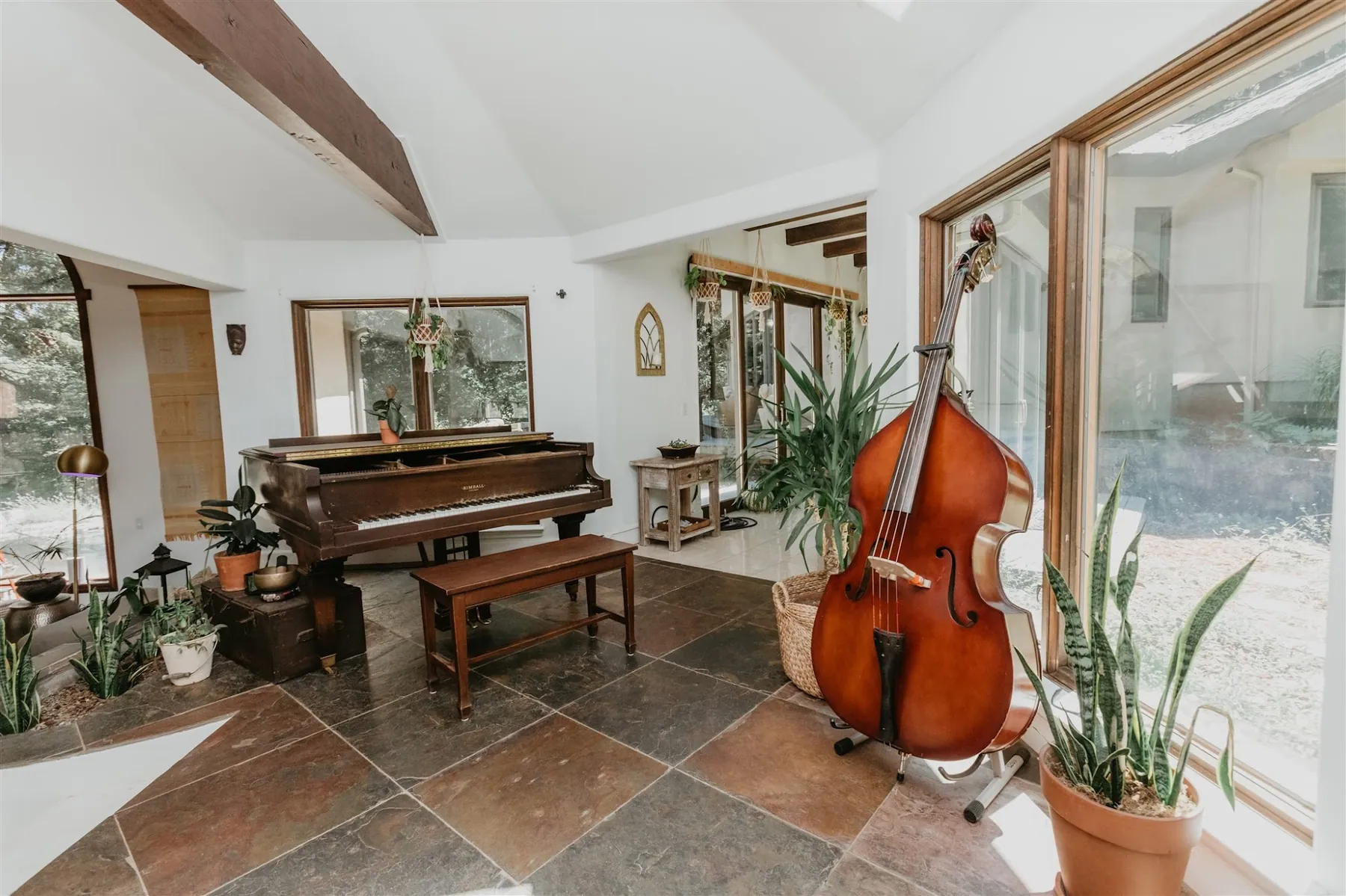 A tiled sunroom with a grand piano and an upright bass beside the windows