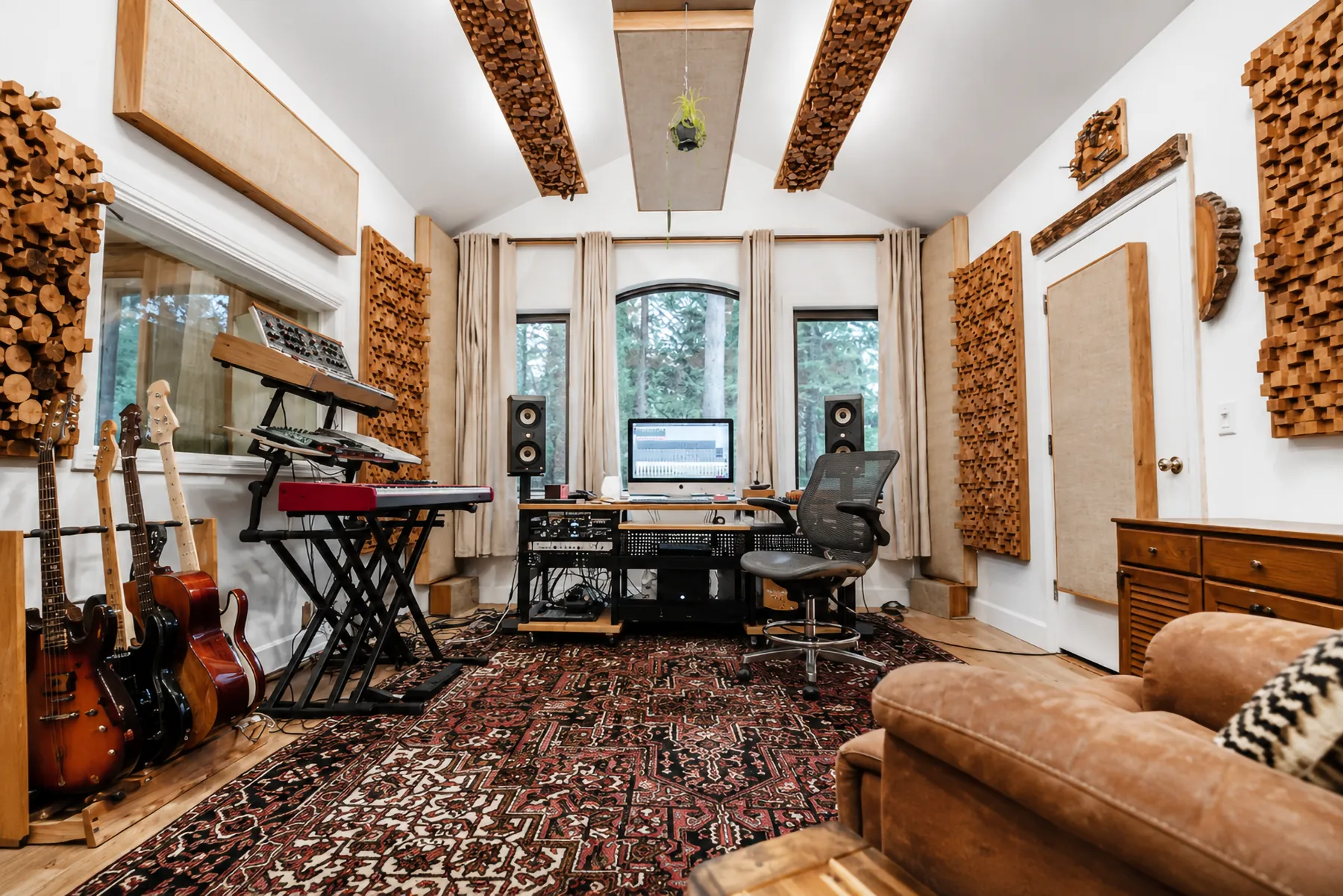 A studio room lined with guitars and acoustic panels, a leather sofa facing the desk