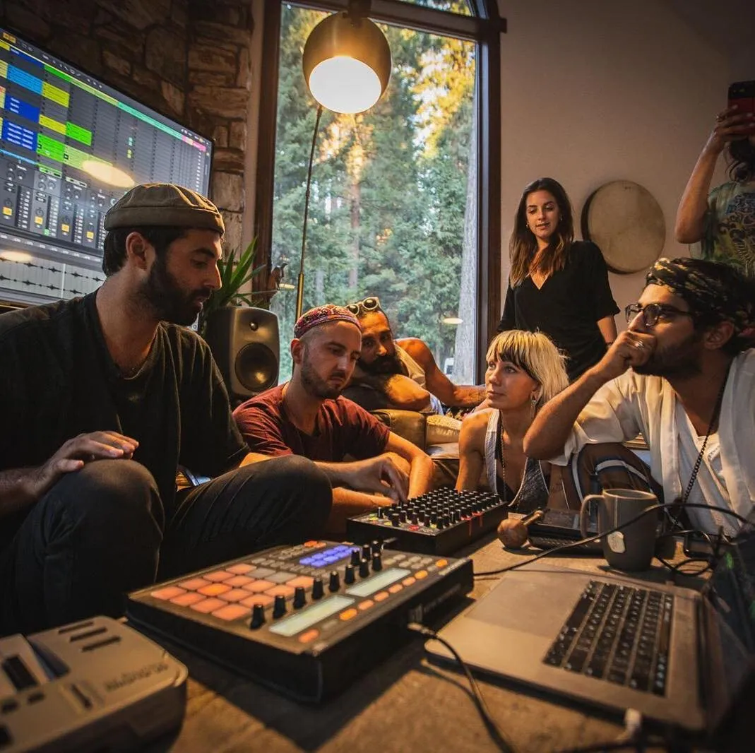 A group gathered around production gear in the studio, forest visible through the window