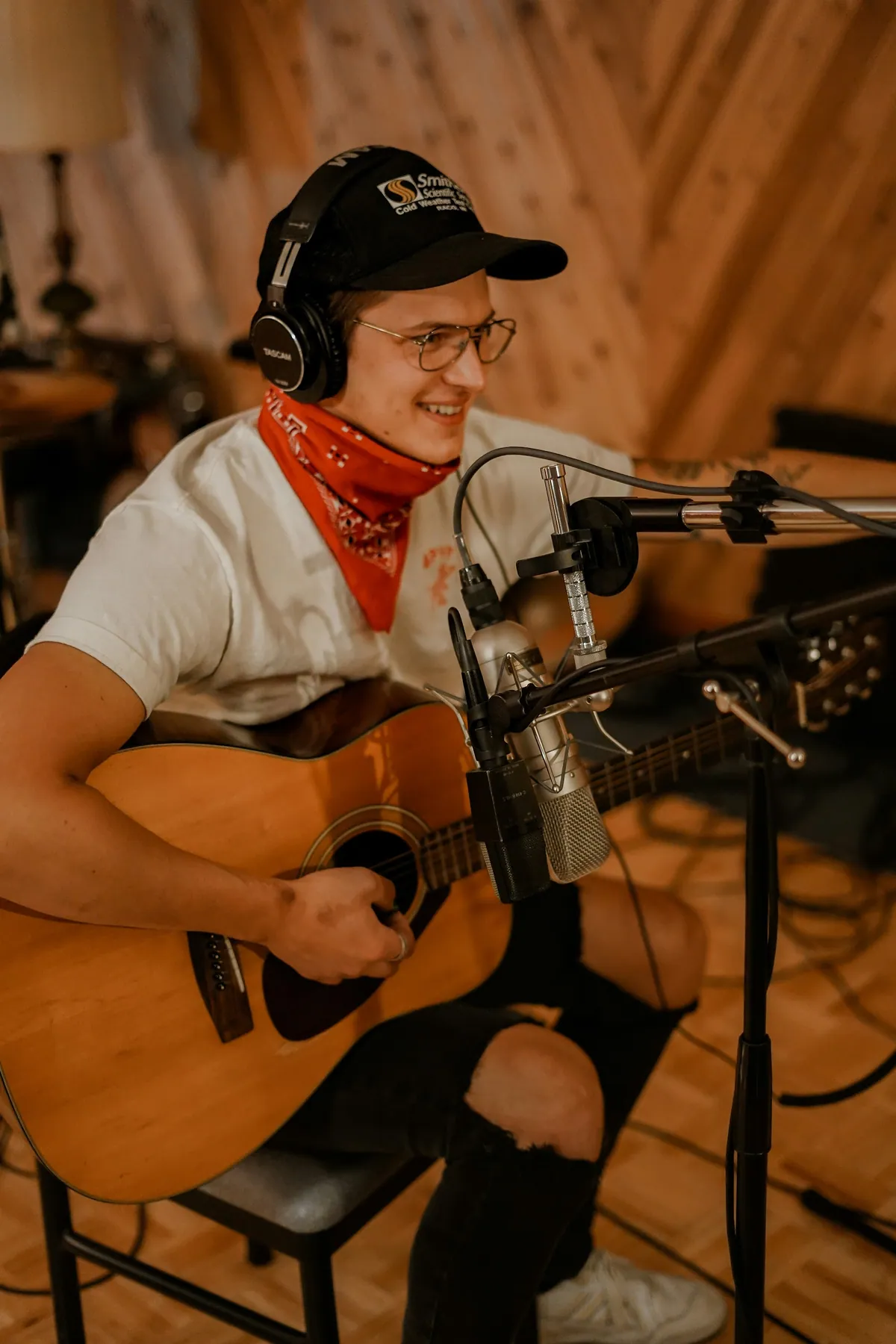 A musician in headphones playing acoustic guitar at a vocal microphone