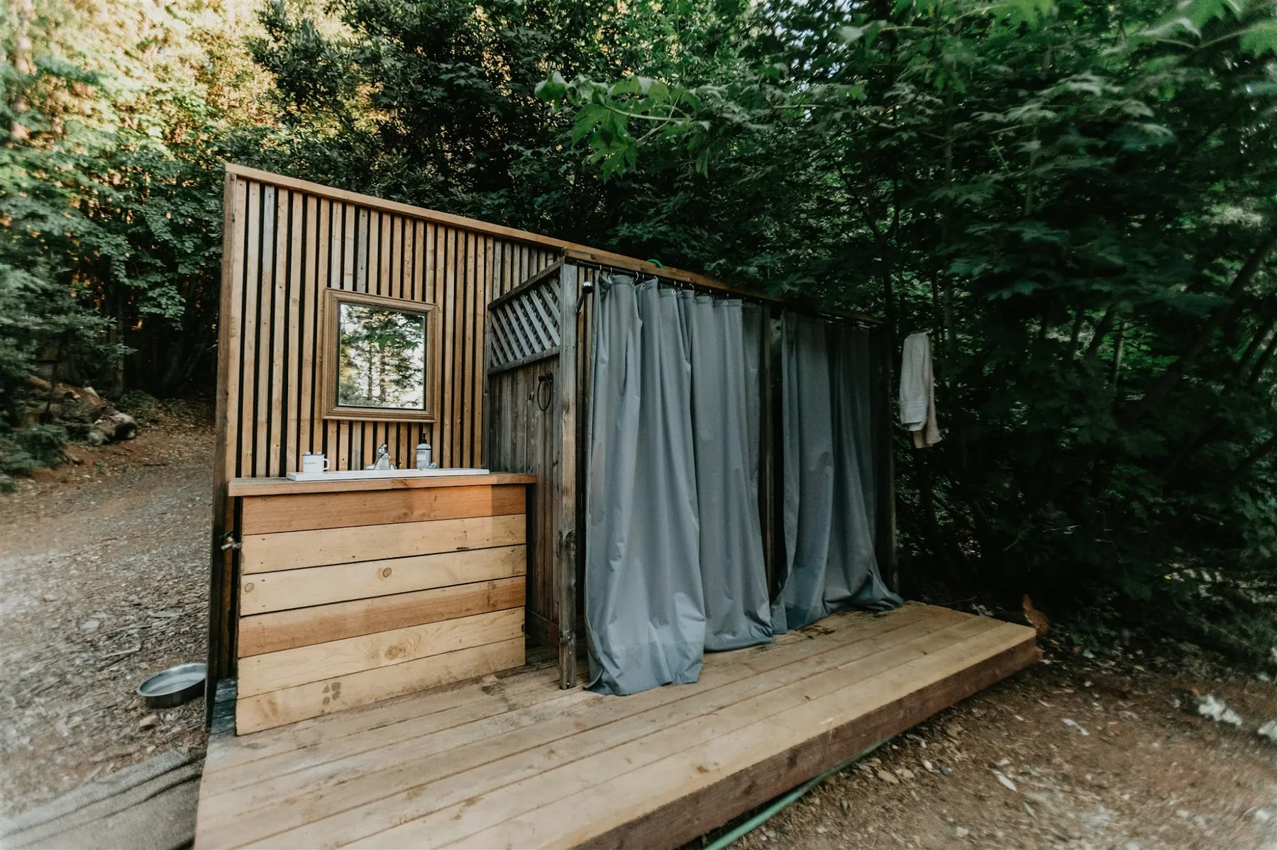 The outdoor shower enclosure in cedar, with a vanity and curtain on a wooden deck