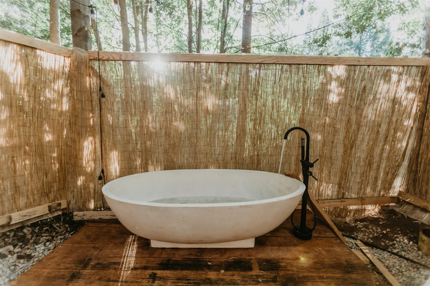 A freestanding outdoor soaking tub on a wooden deck behind a reed privacy screen