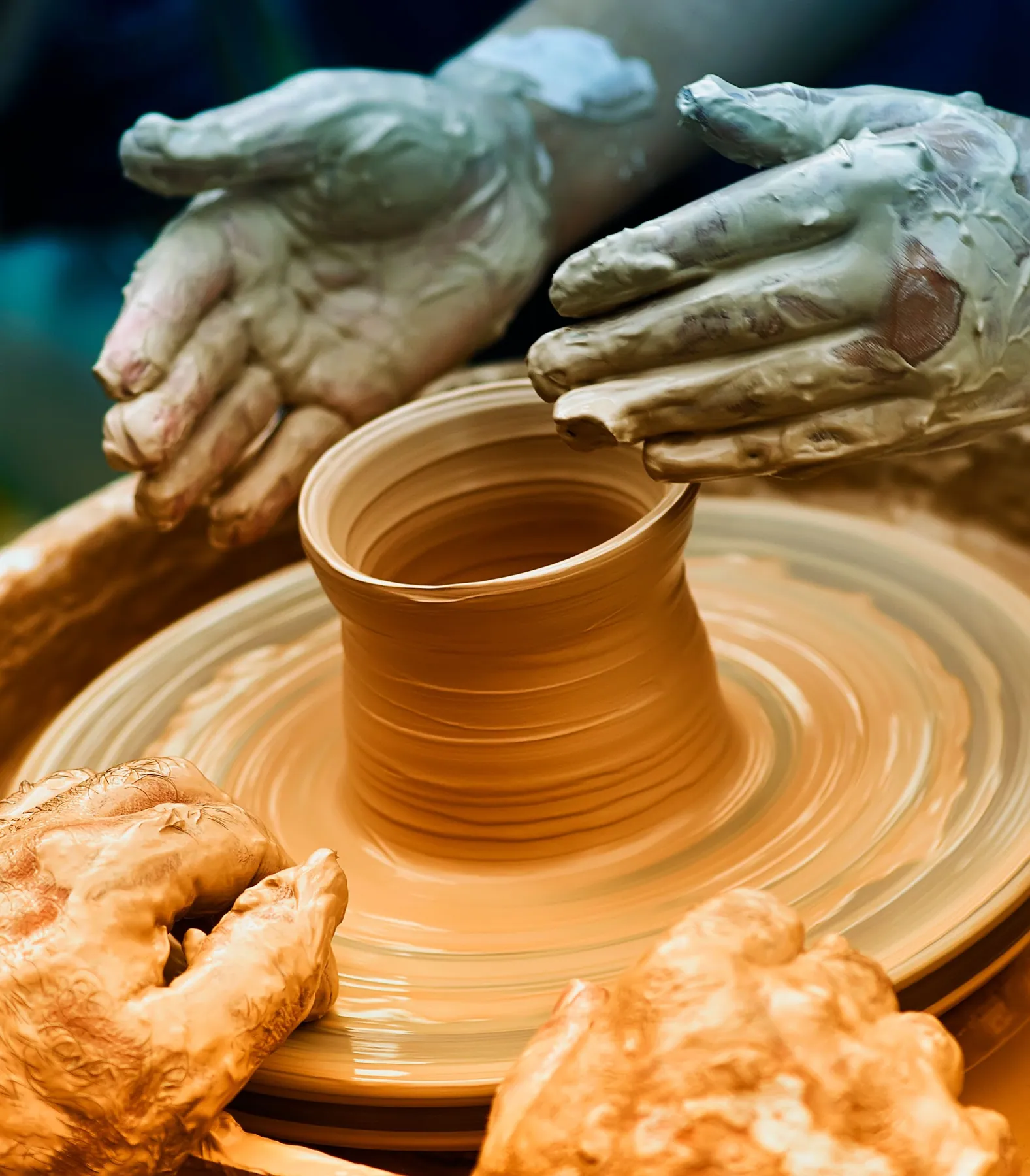 Hands shaping a clay vessel on a potter's wheel