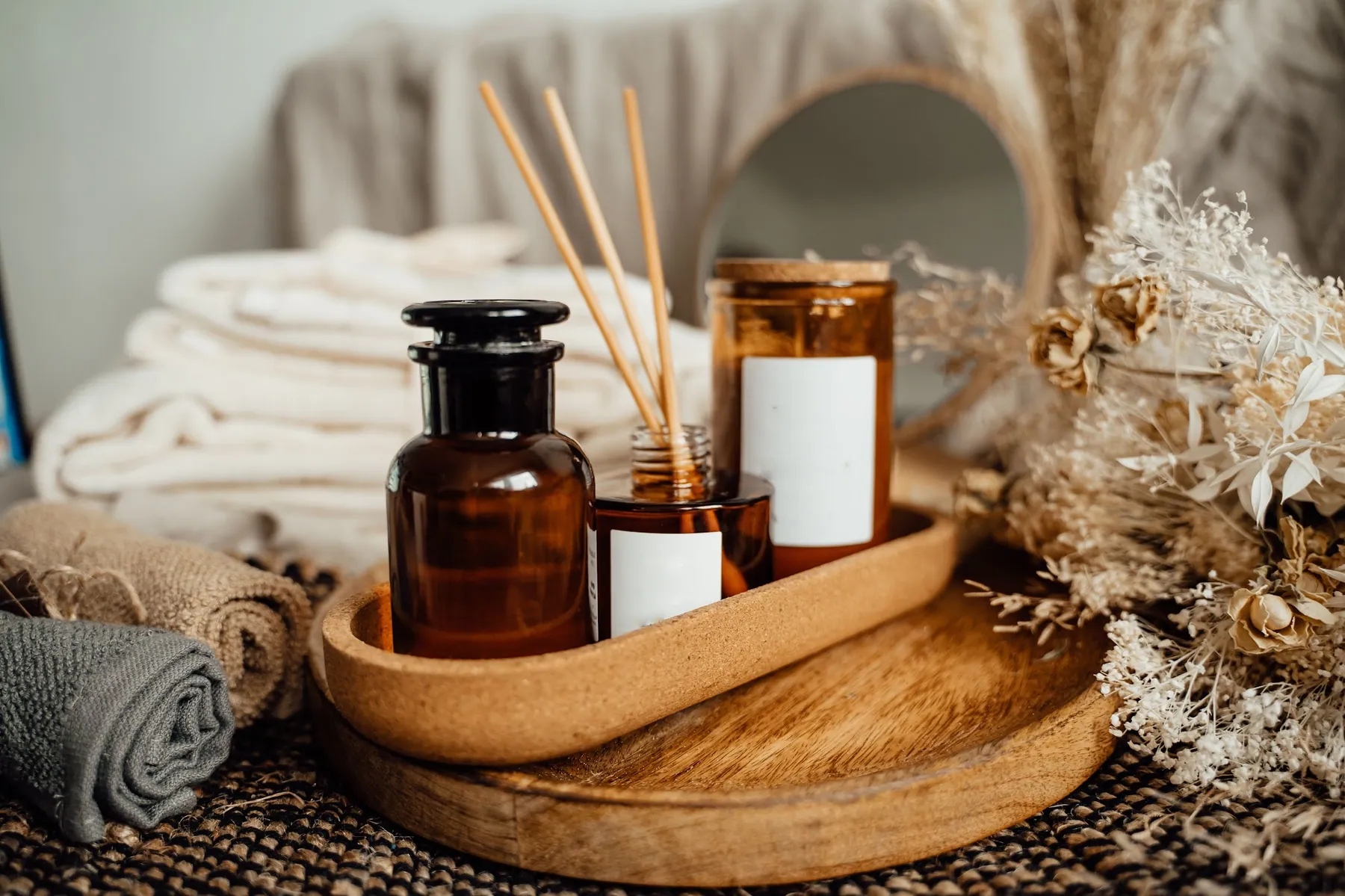 Amber apothecary bottles, a reed diffuser and rolled towels arranged on a wooden tray