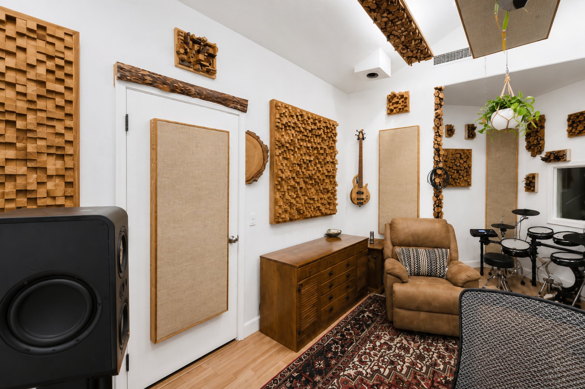 A subwoofer and acoustic panels beside the booth door, drums in the corner
