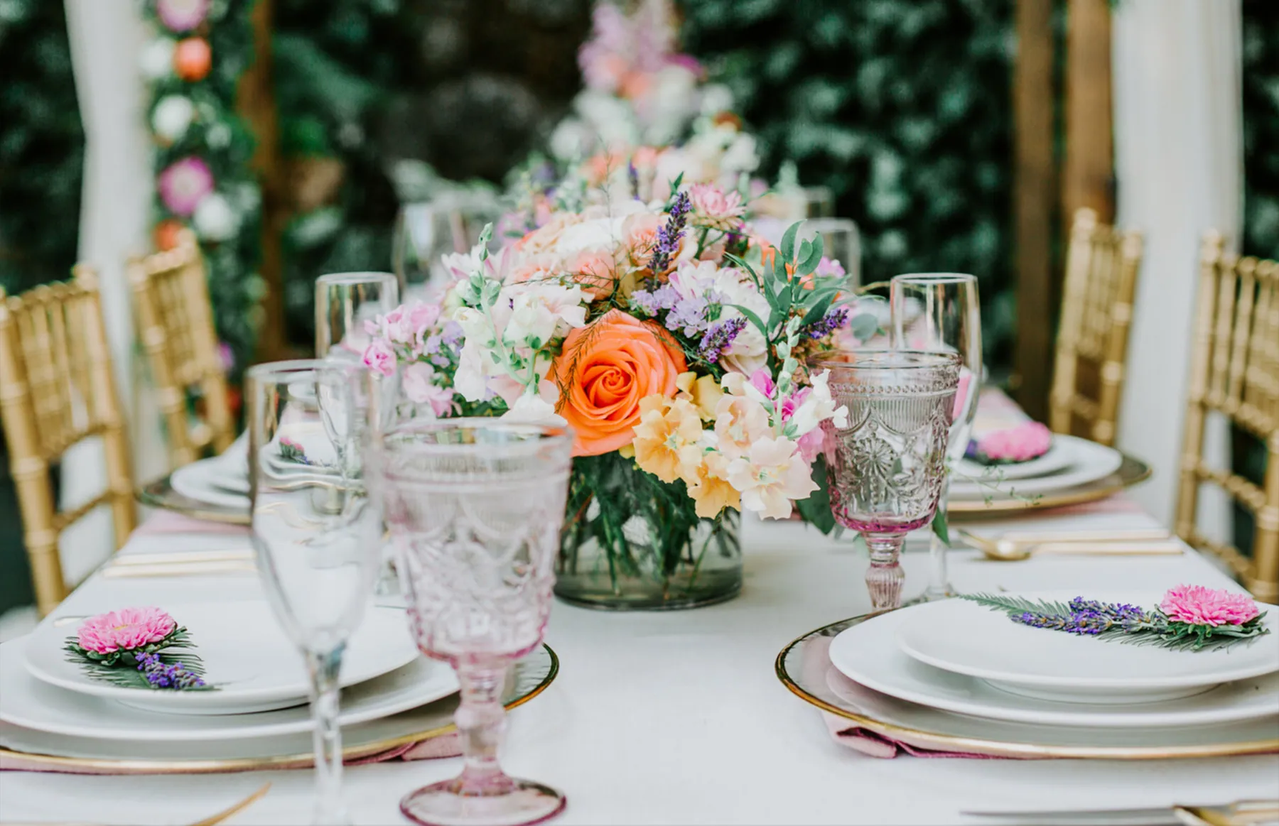 A wedding reception table set with spring florals, coloured glassware and gold chairs